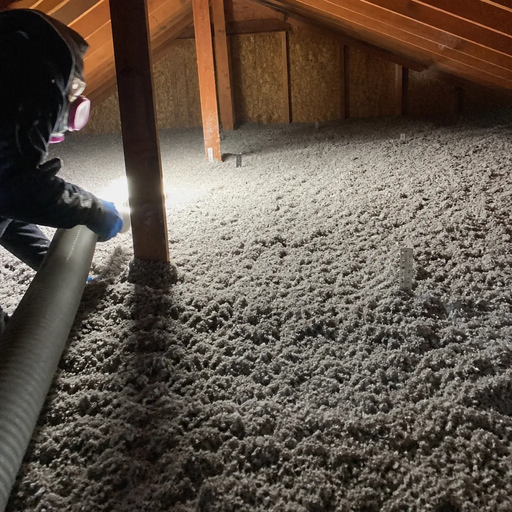 Technician installing blown-in cellulose insulation in an attic